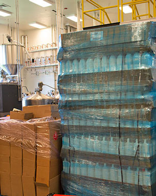 Pallets stacked with gallon containers of Gervasi Vineyard hand sanitizer in a distillery production facility, ready for public distribution.